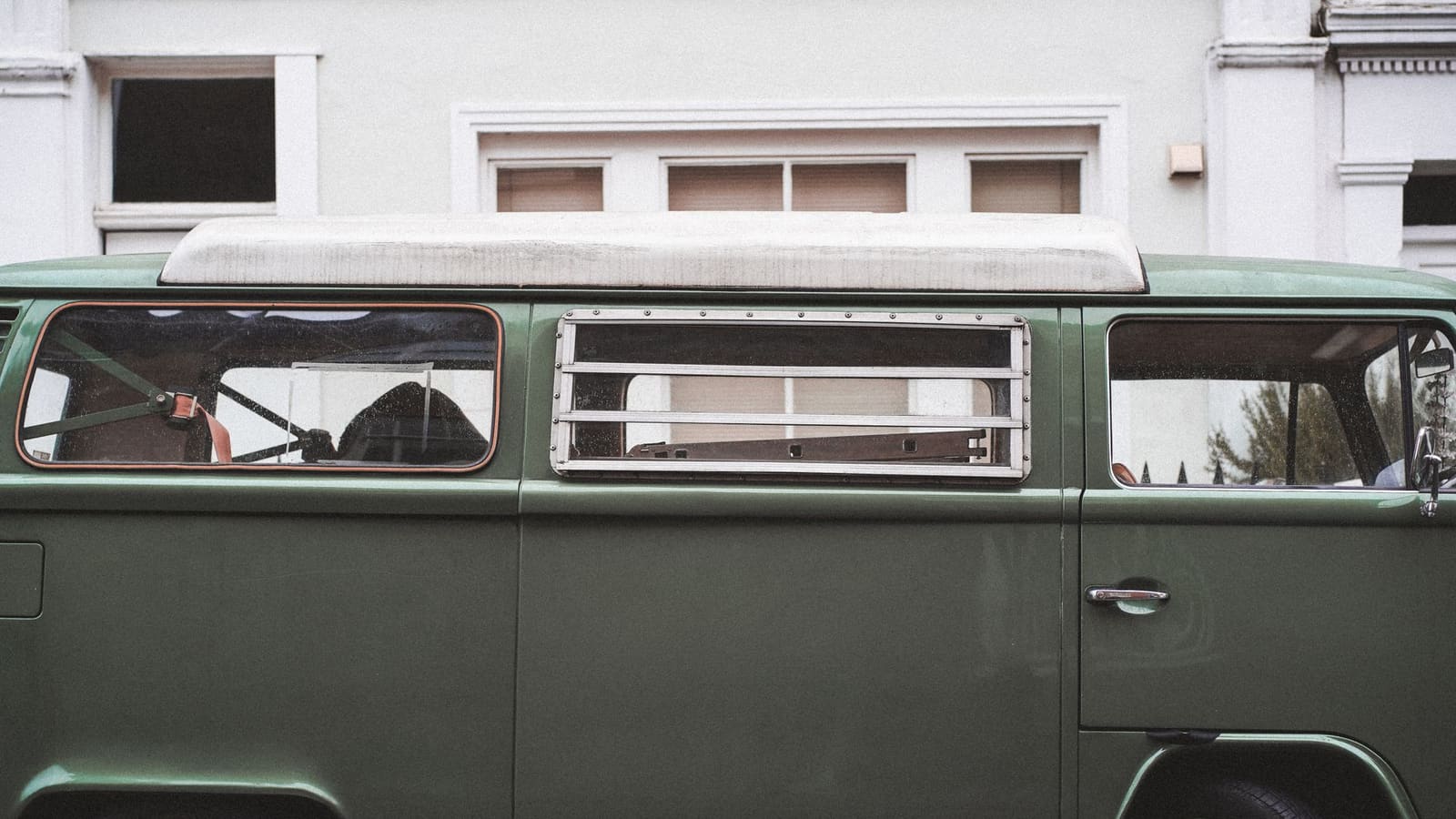 A dark green van parked on a street in front of a pale painted townhouse